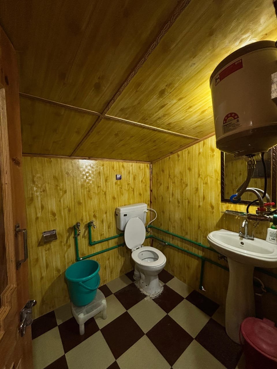 Clean attached bathroom with hot water geyser, toilet and sink, wooden walls