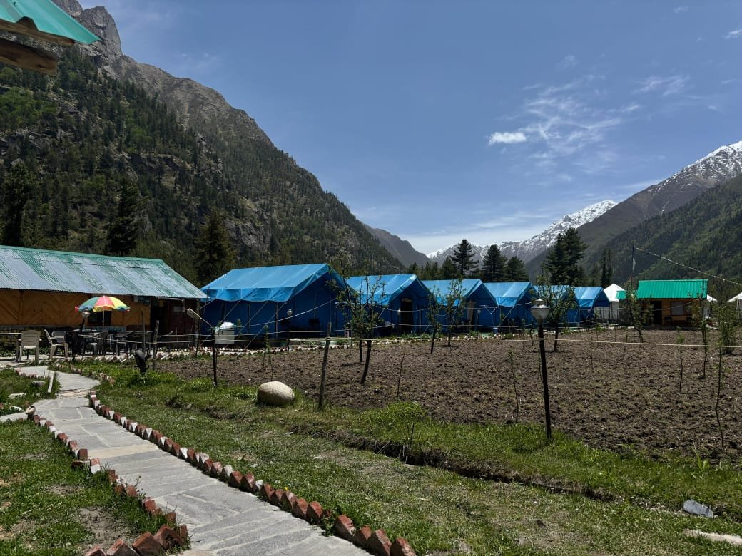Row of blue Swiss tents with dining umbrella and Himalayan mountains in the background